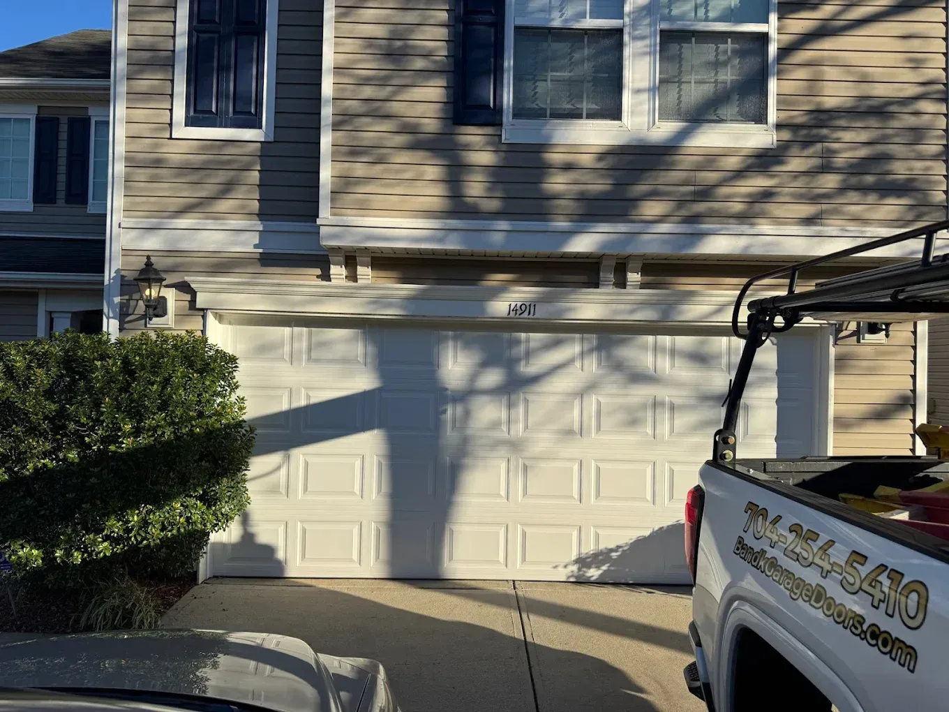 Suburban house front with two garage doors, driveway, and a white pickup truck in sunlight