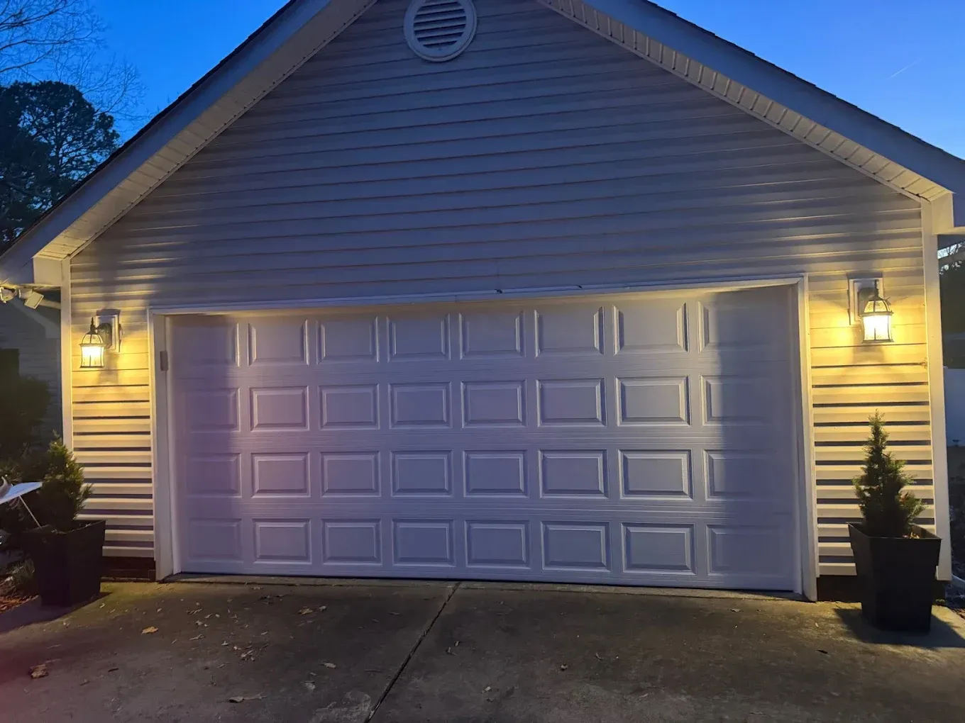 Suburban garage with a white door lit by warm exterior lights at dusk