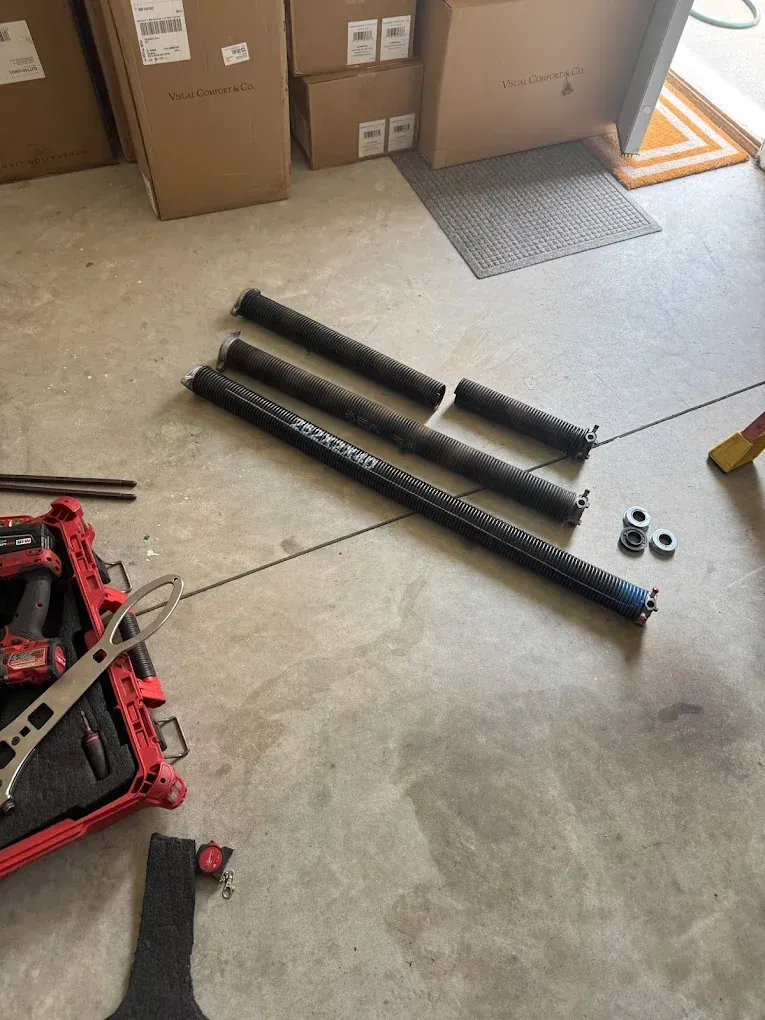 Garage floor with black cylindrical parts, a red toolbox, and stacked cardboard boxes near a door.