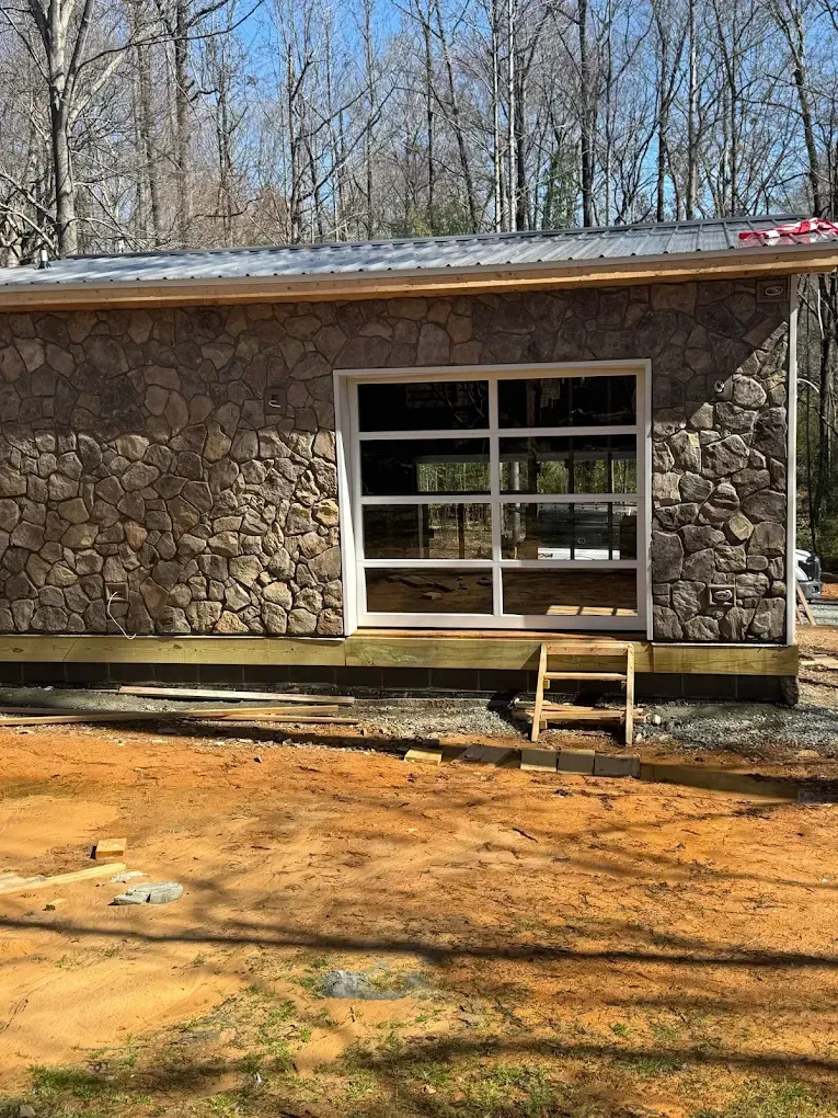 Stone building wall with a white-framed window and small step ladder on bare dirt outdoors