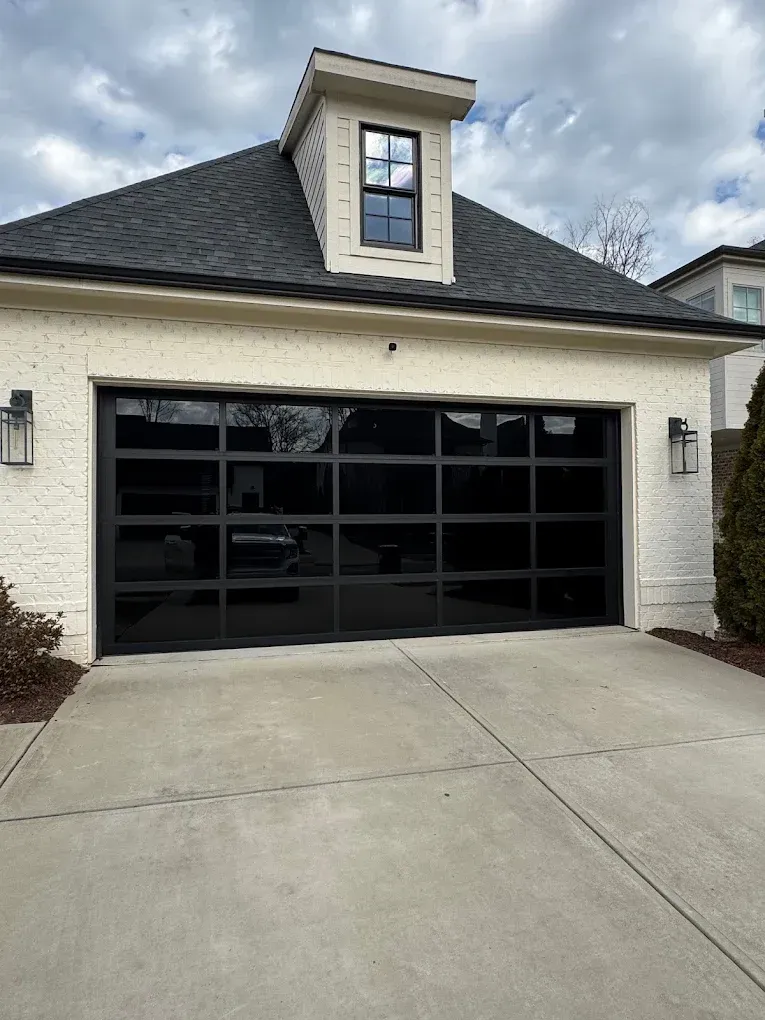 Black garage door on a white brick house with a small dormer window above the driveway.