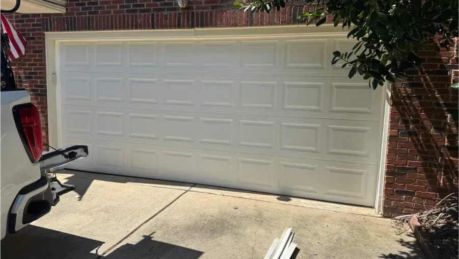 White double garage door on a brick house, with a driveway and part of a parked vehicle visible.