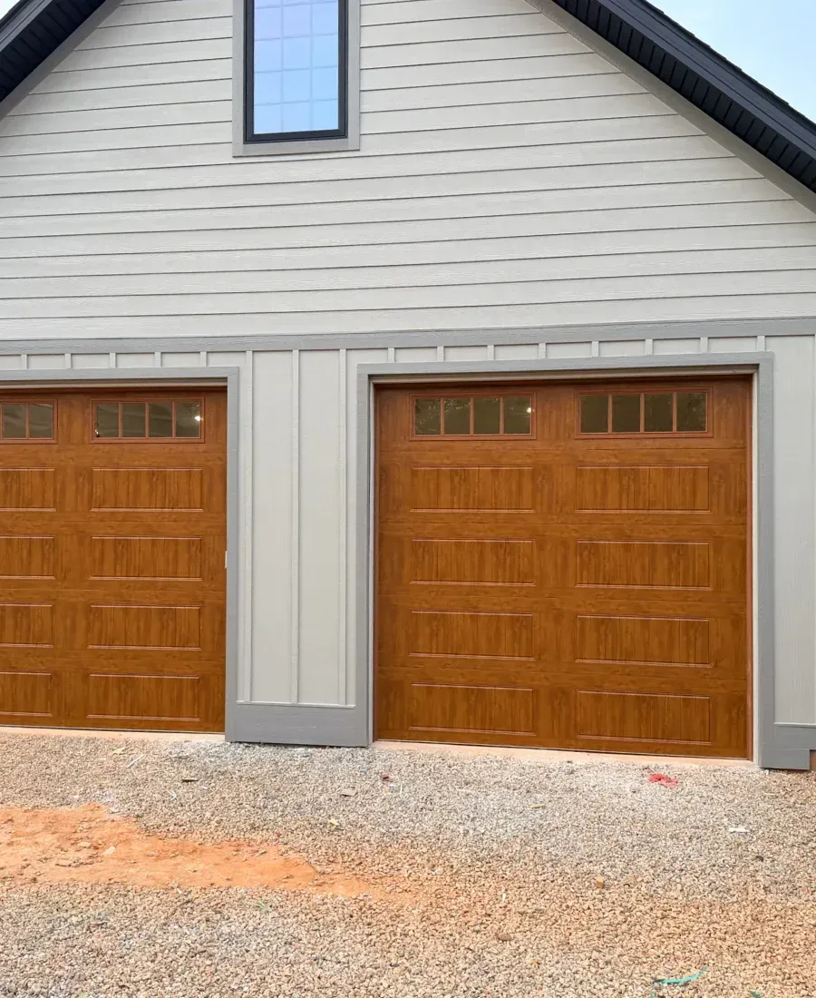 Two brown wooden garage doors on a beige house with gray trim and gravel driveway