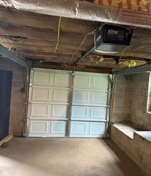 Dim garage interior with a closed white paneled door and exposed ceiling beams.
