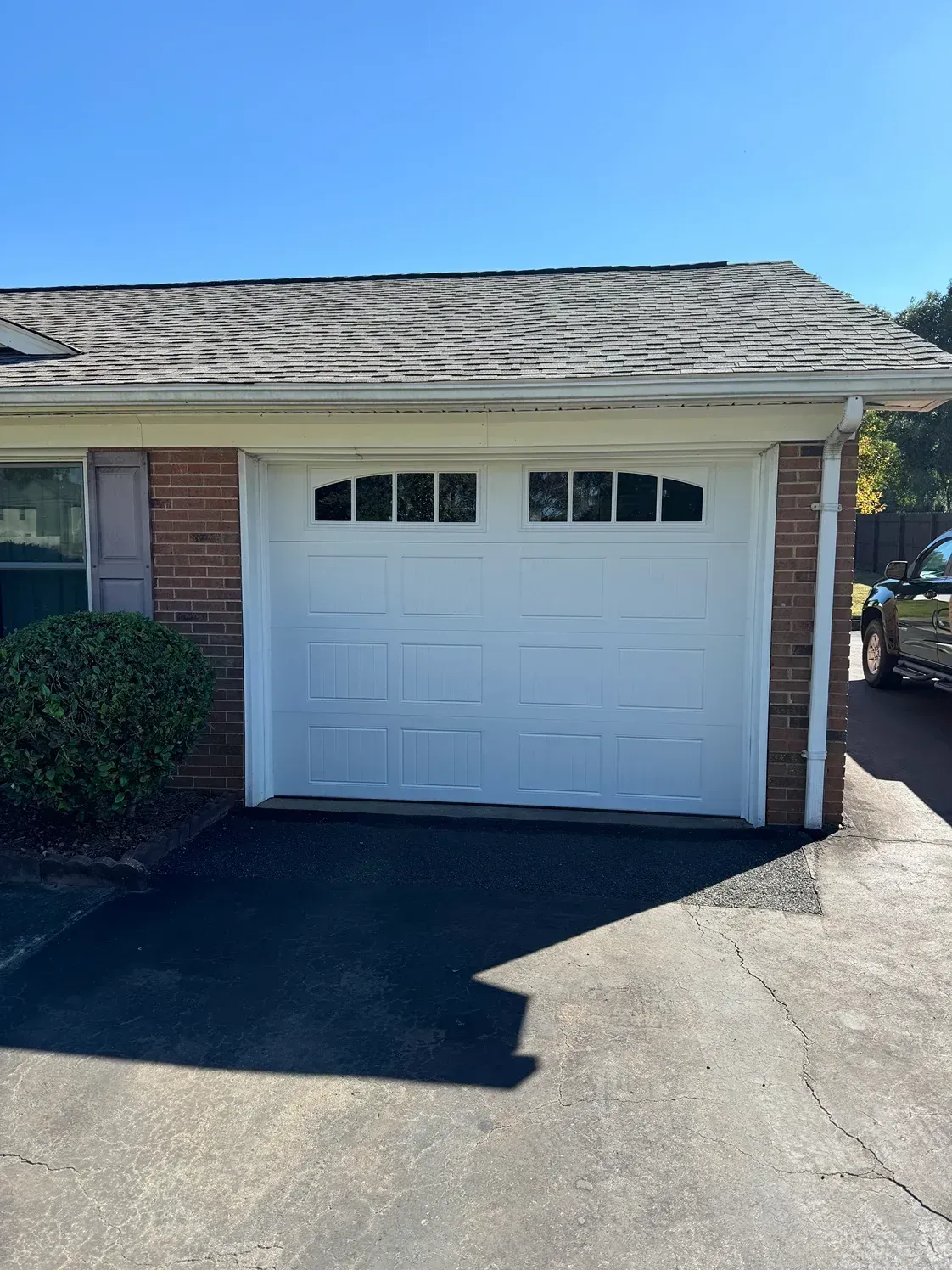 White garage door on a brick house with a dark driveway and clear blue sky