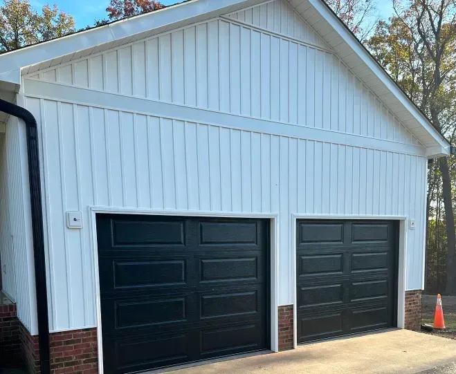 White detached garage with two black doors and a peaked roof on a driveway