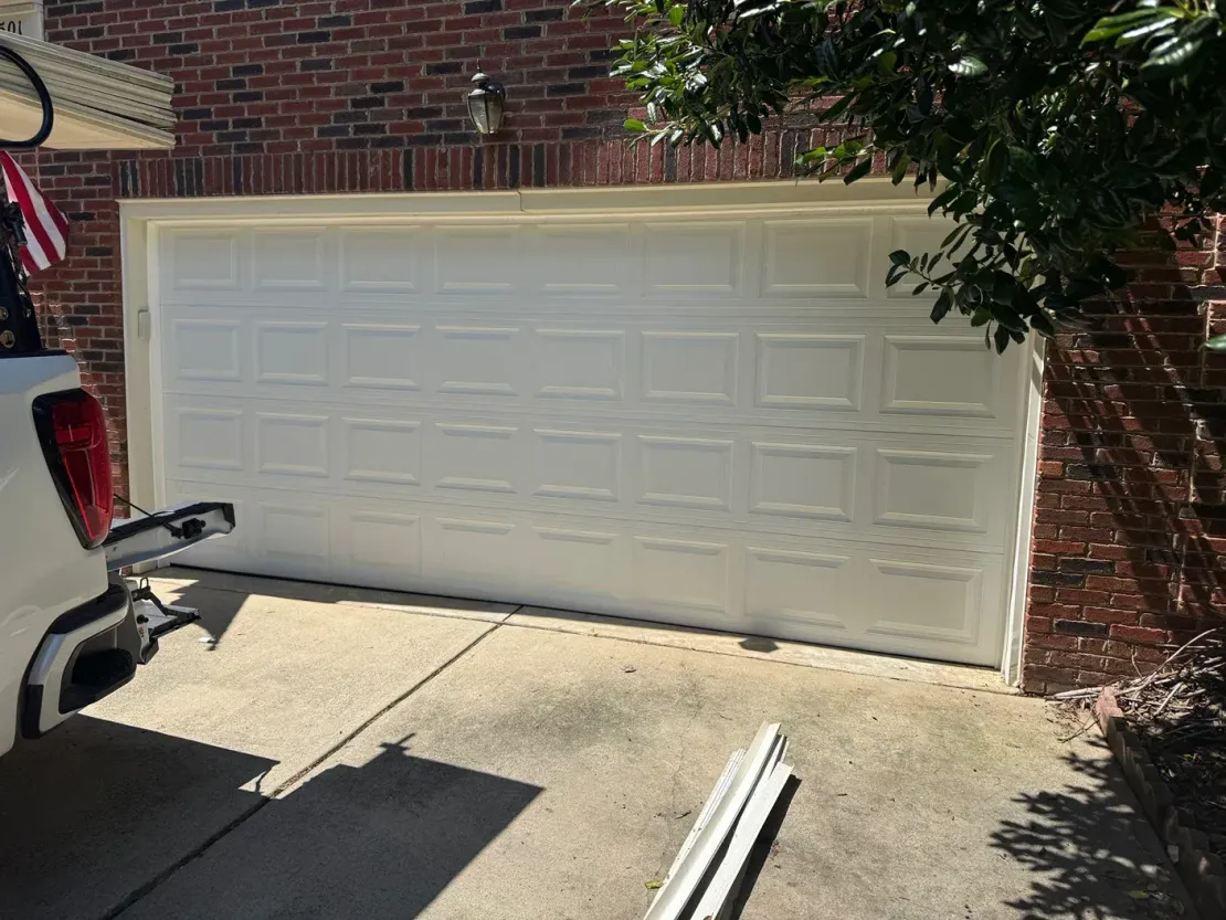 White garage door on a brick house with a car trailer hitch visible at left and a driveway in front.