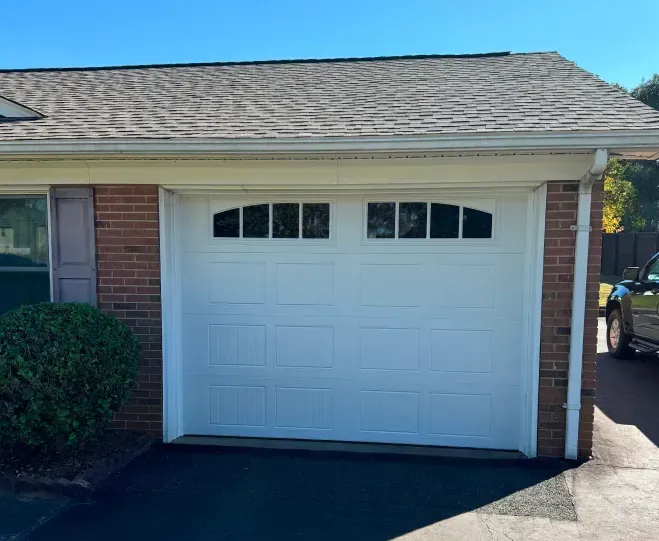 White single-car garage door on a brick house with shingled roof and driveway in front