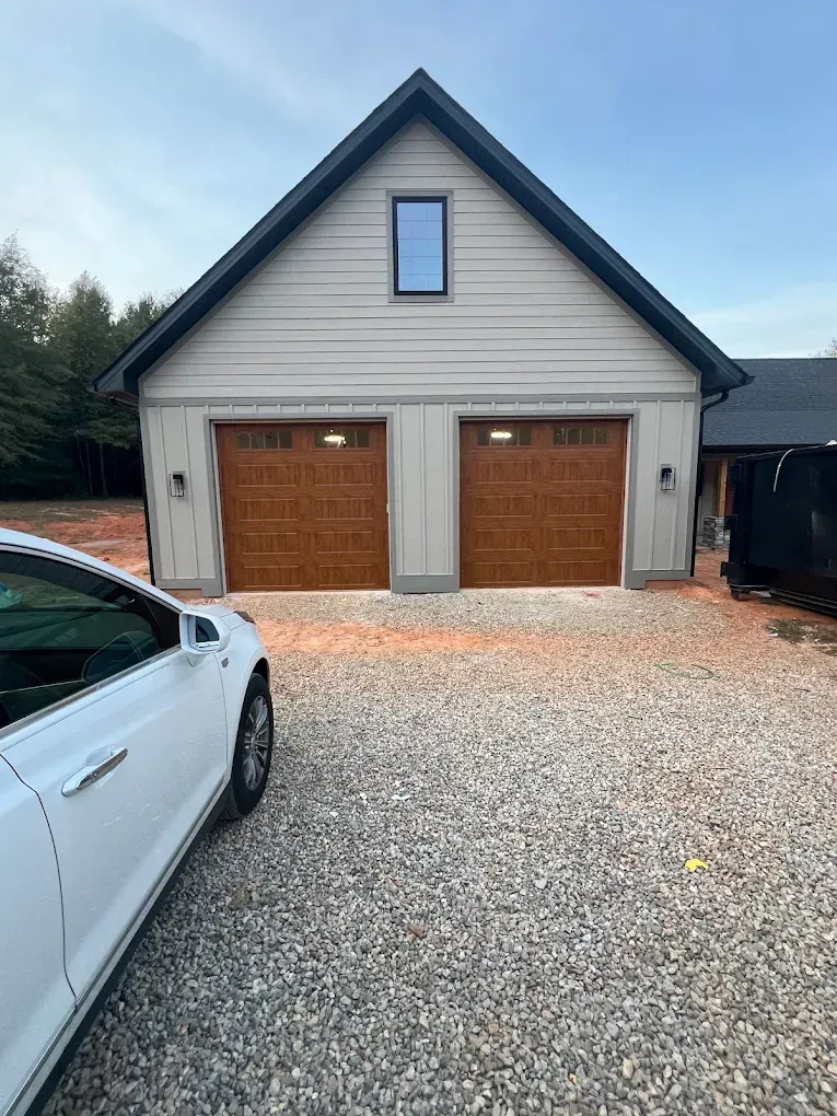 Two-car garage with brown doors, gravel driveway, and a white car parked on the left.