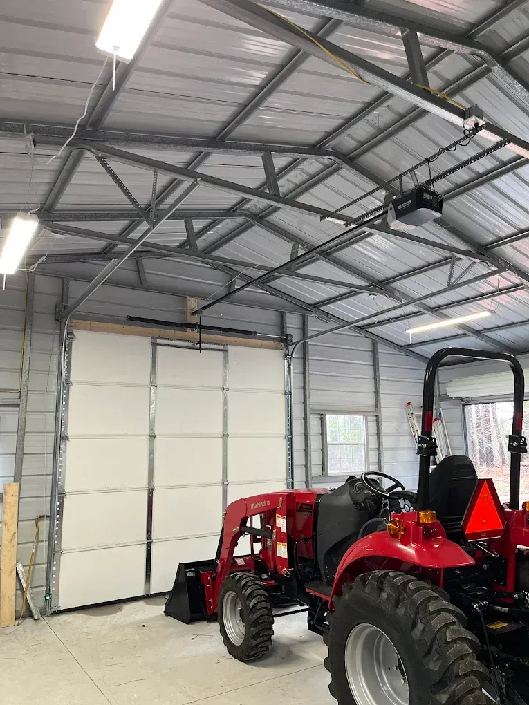 Red tractor in a metal garage with a white roll-up door and concrete floor