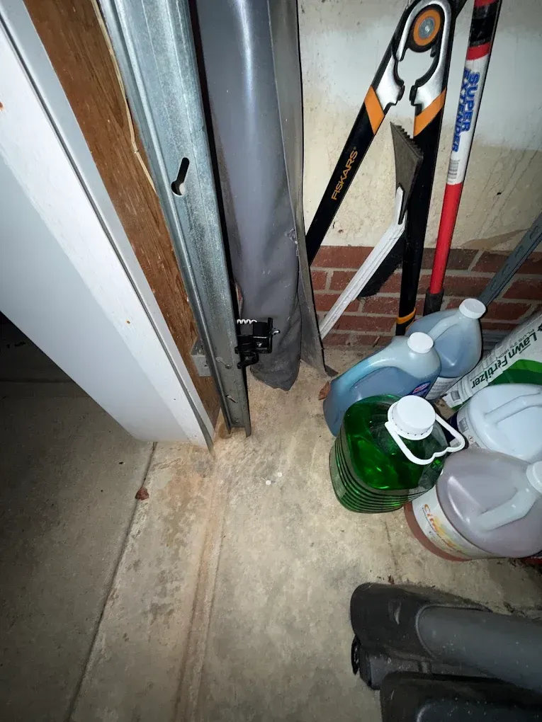 Cluttered storage corner with a metal cabinet, tools, a green basket, plastic jugs, and a floor fan.