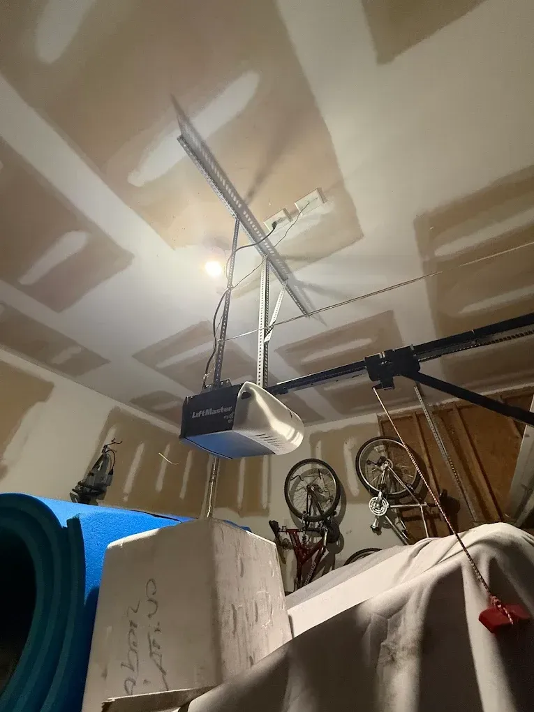 Garage ceiling with a hanging door opener, exposed rafters, and stacked boxes and wheels below