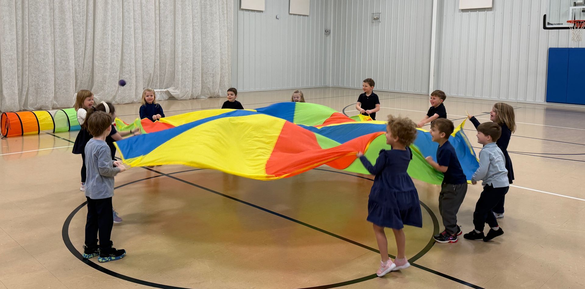 Children holding a colorful parachute in a gymnasium during a group play activity