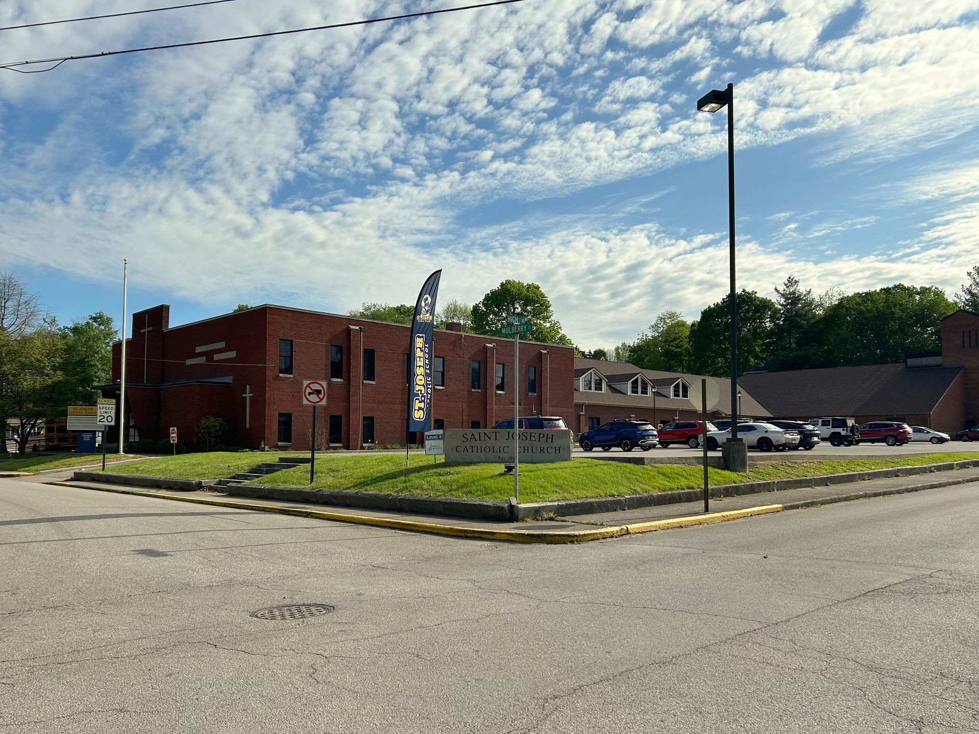 Brick building at a street corner with parked cars, trees, and a cloudy sky
