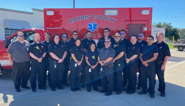 A group of paramedics are posing for a picture in front of an ambulance.