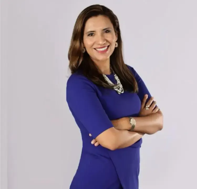 A woman in a blue dress is smiling with her arms crossed