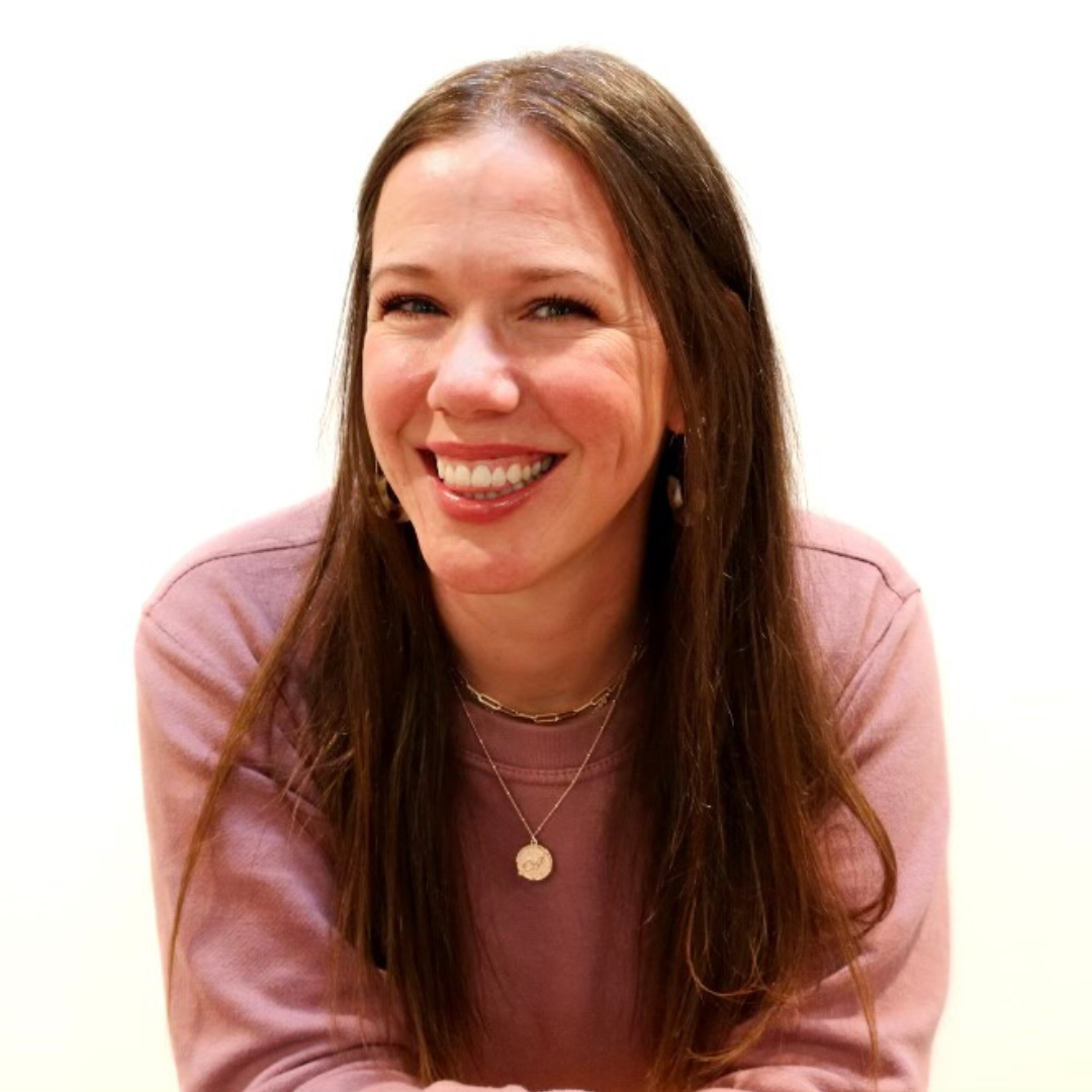 A woman wearing a pink sweater and a necklace smiles for the camera