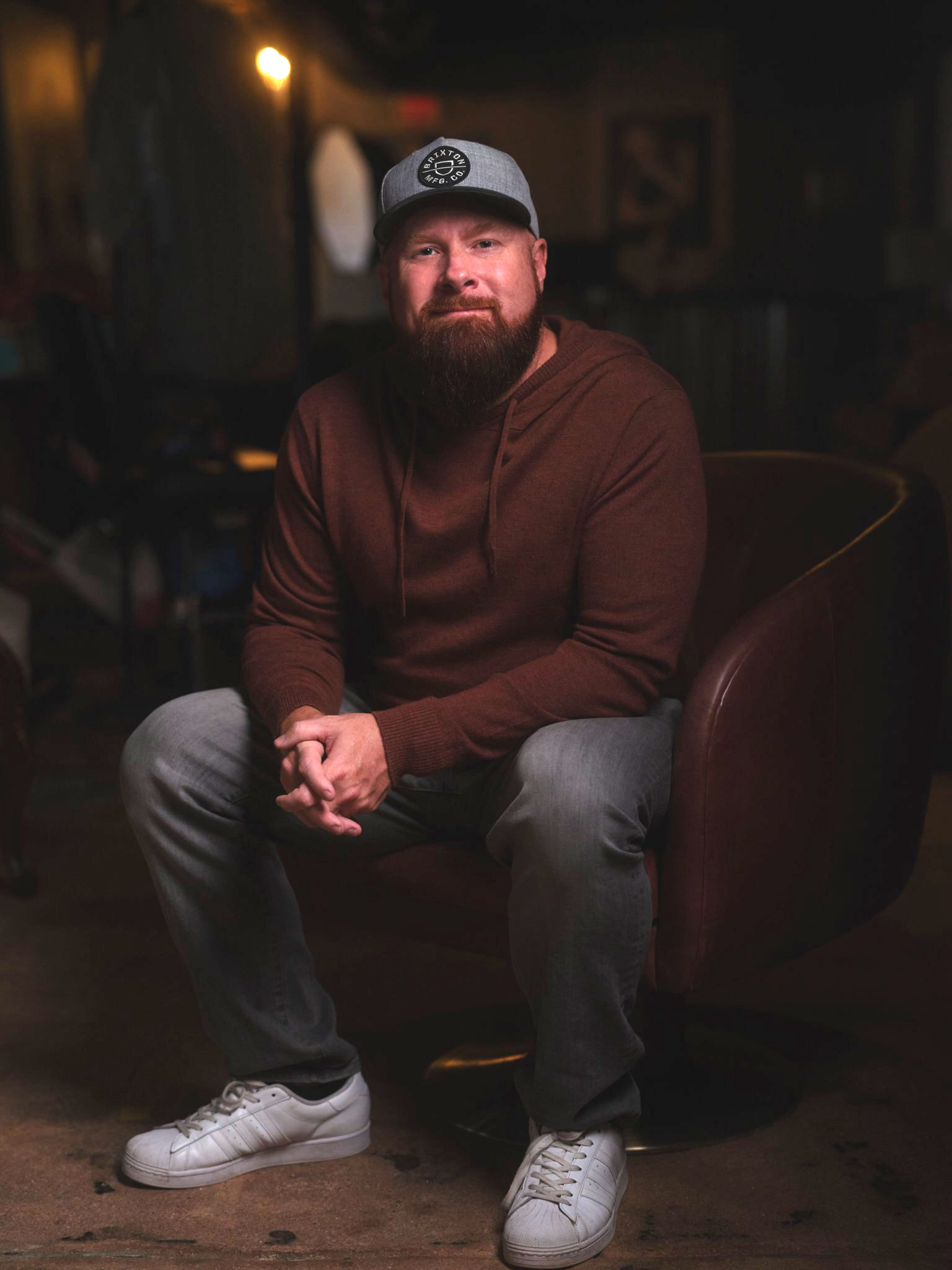 A man with a beard is sitting in a chair wearing a hat.