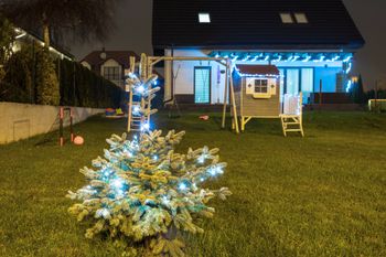 A Christmas tree is sitting in the grass in front of a house at night.