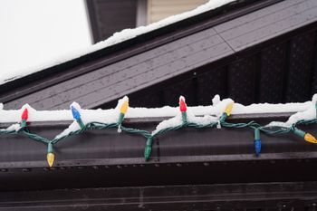 A string of christmas lights hanging from a gutter covered in snow.