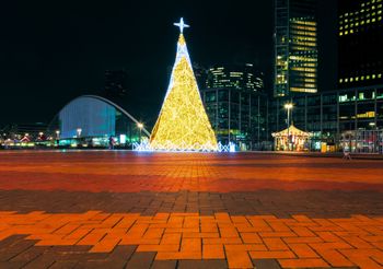 A large Christmas tree is lit up in a city at night