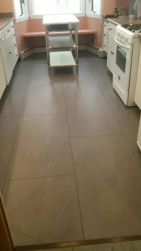 Kitchen with large brown tile floor, white stove on the right, and a metal cart centered between counters.