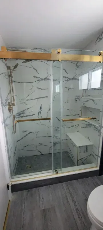 Modern walk-in shower with glass doors, marble-look tile, and two wooden shelves
