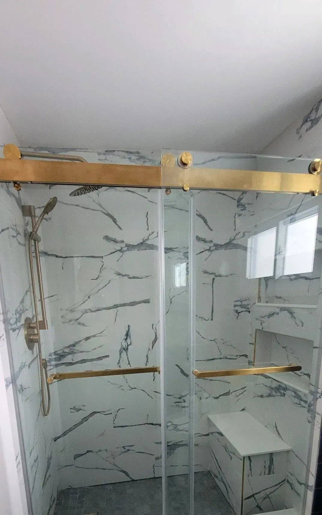 Bathroom shower with marble-pattern tile, glass enclosure, and a white sink on the right.