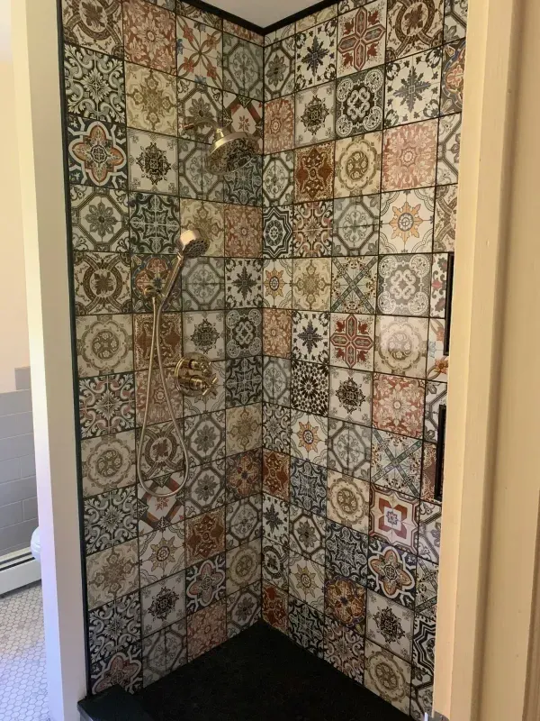 Tiled shower alcove with patterned multicolor wall tiles and a dark floor drain