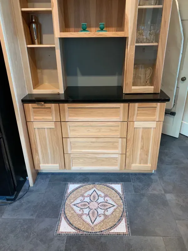 Light wood entertainment cabinet with black countertop and decorative tile medallion on dark floor in a room