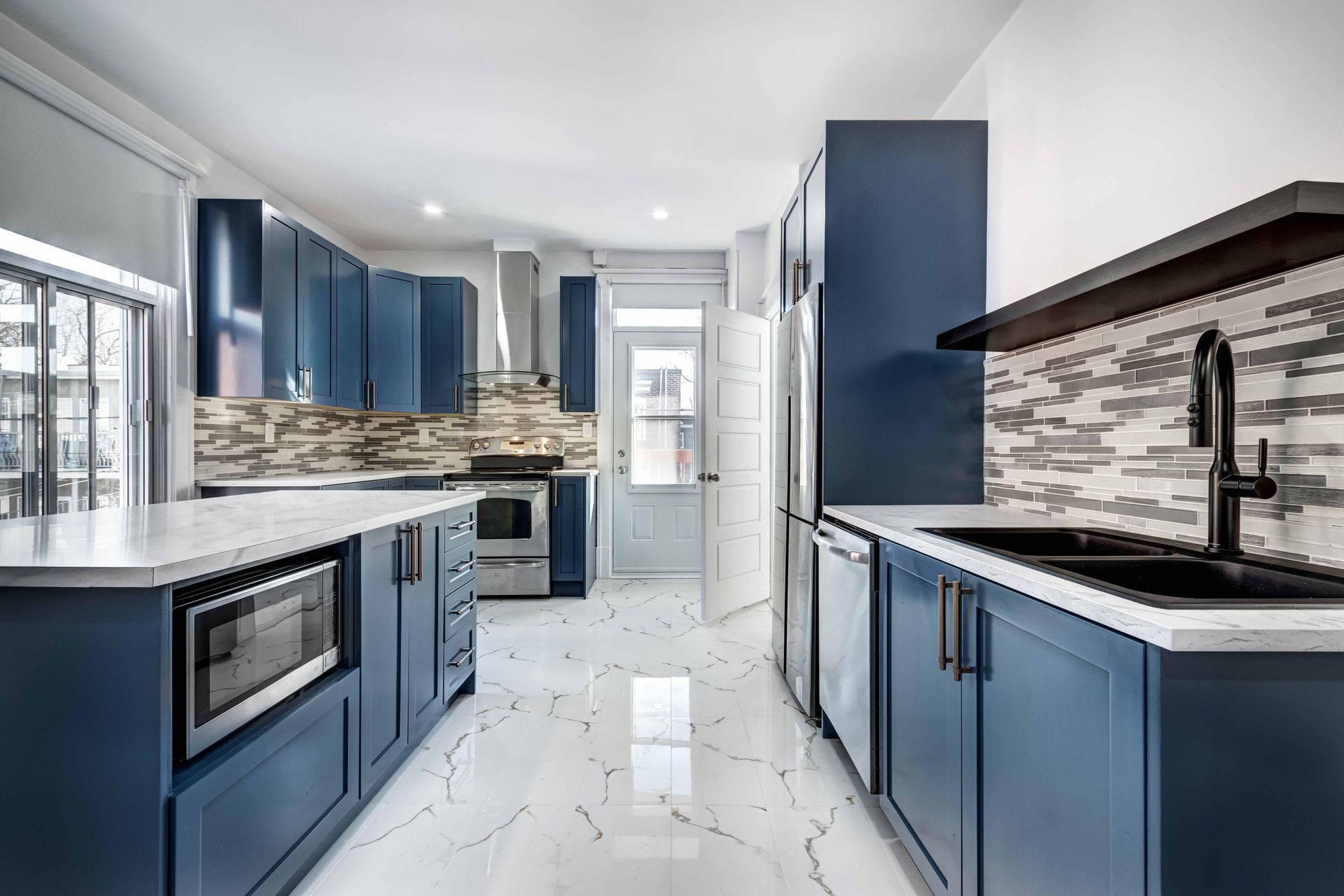 Modern kitchen with blue cabinets, marble-look countertops, stainless steel appliances, and white tile floor