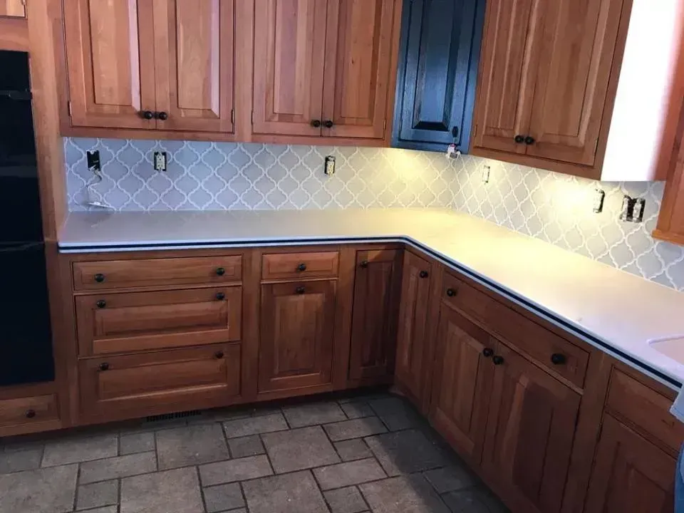 Wooden kitchen cabinets, white countertop, and tiled backsplash in an empty kitchen