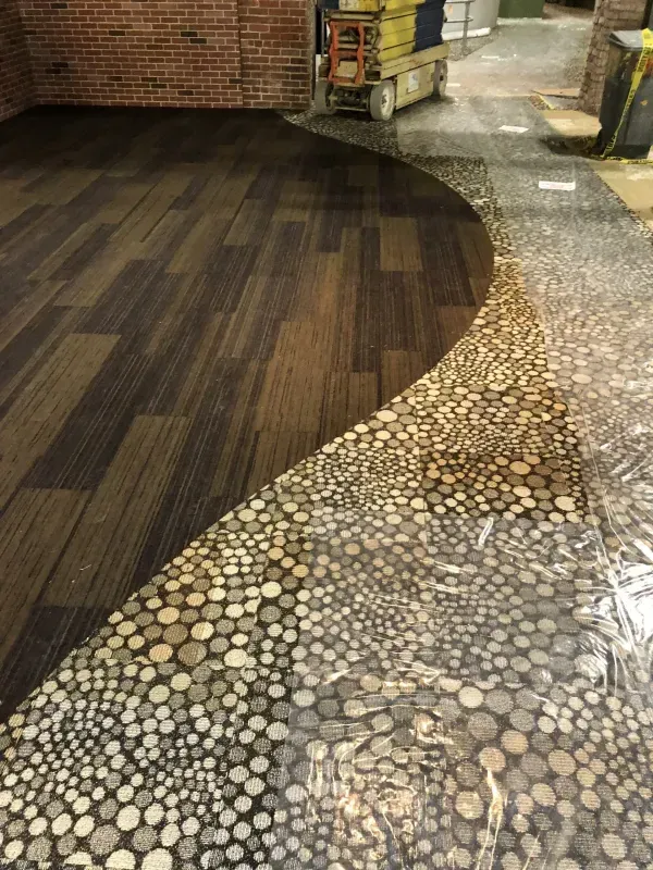 Curved flooring transition from dark wood planks to pebble mosaic in an indoor space