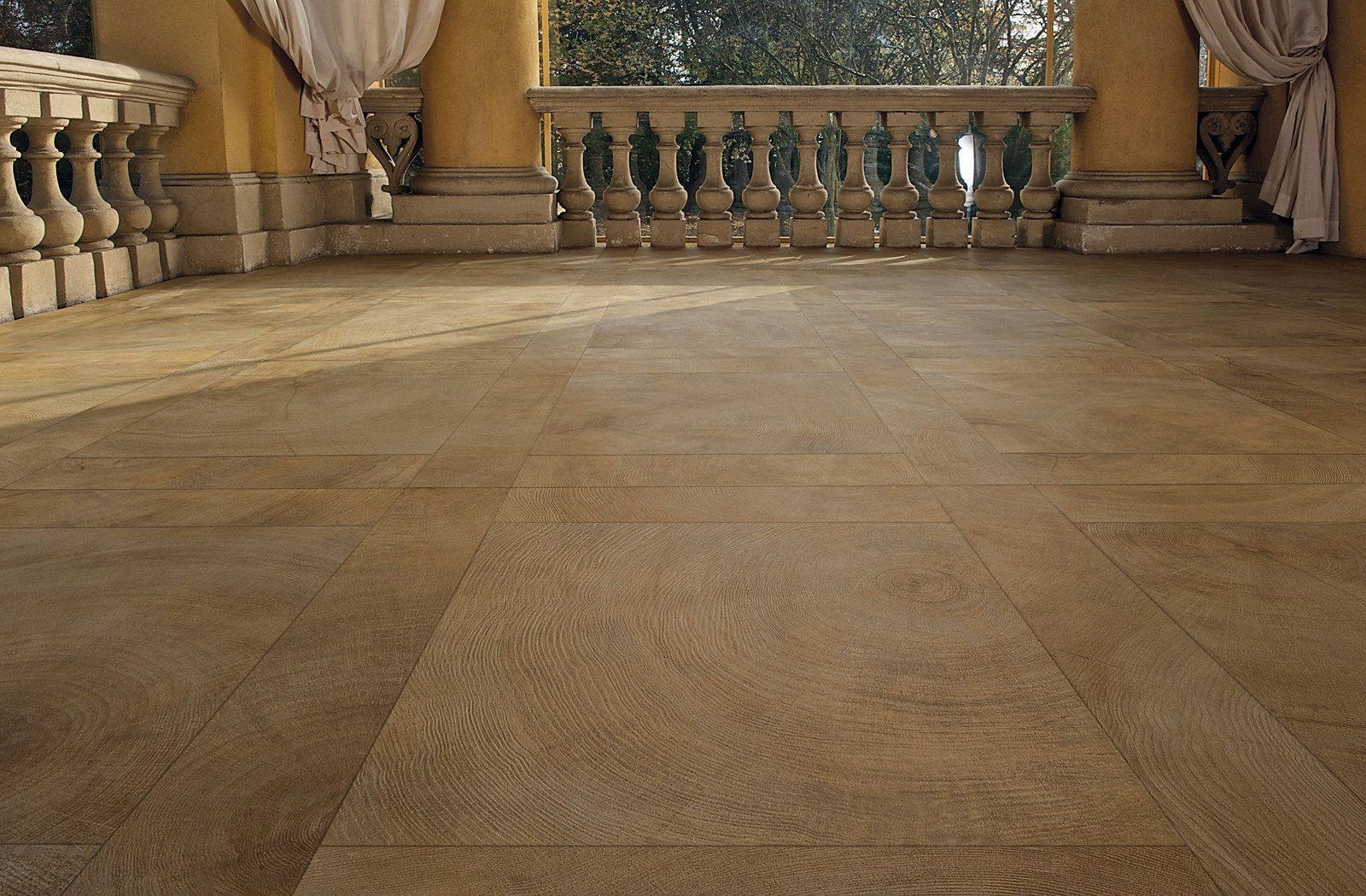 Stone terrace with balustrades and draped curtains overlooking greenery