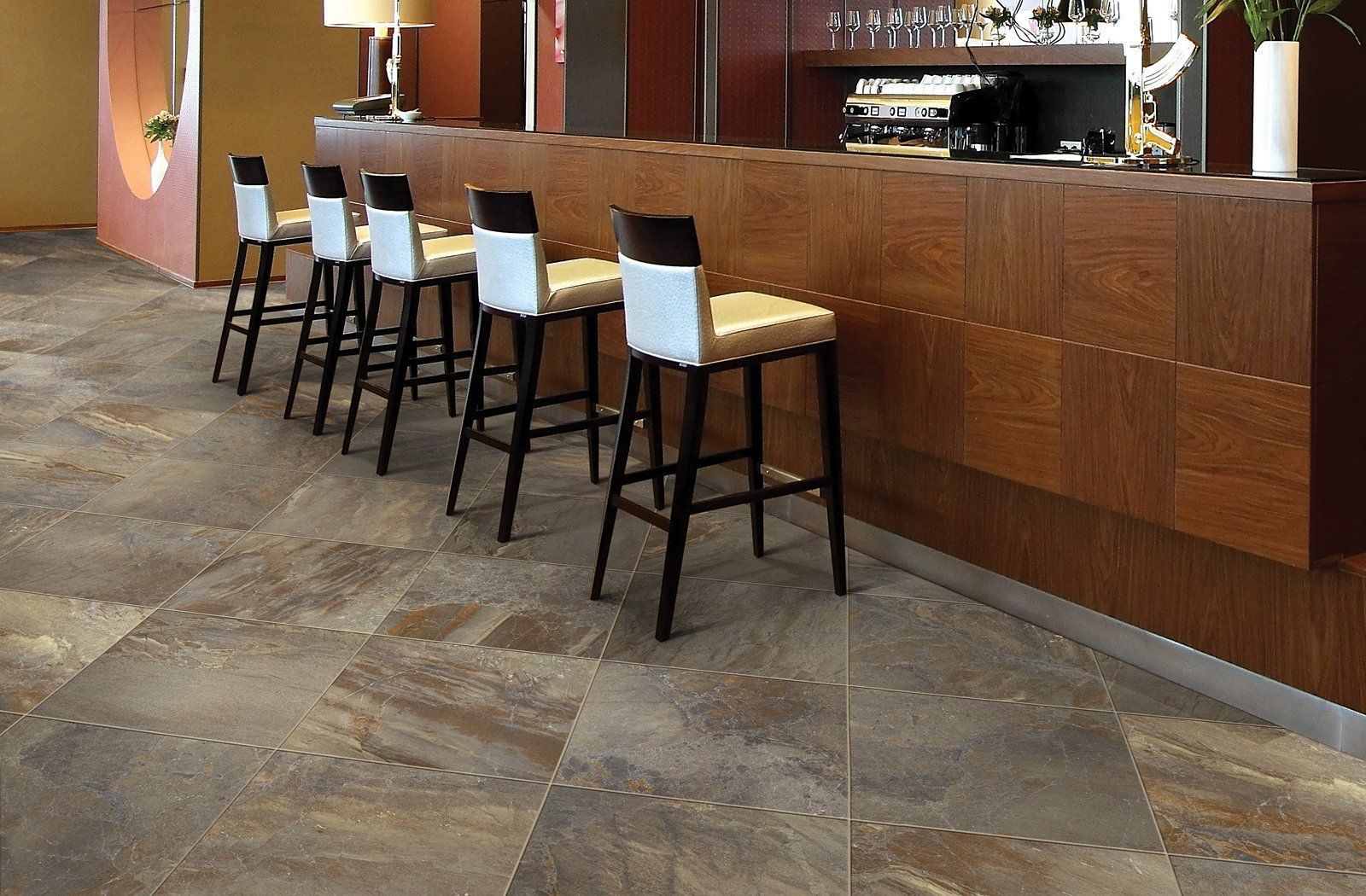 Modern hotel bar with wooden counter and tall stools on a tiled floor.