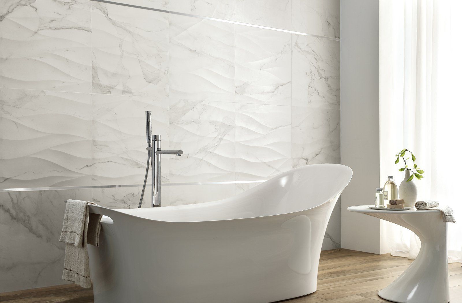 Modern white bathtub in a bright bathroom with marble walls and a small side table