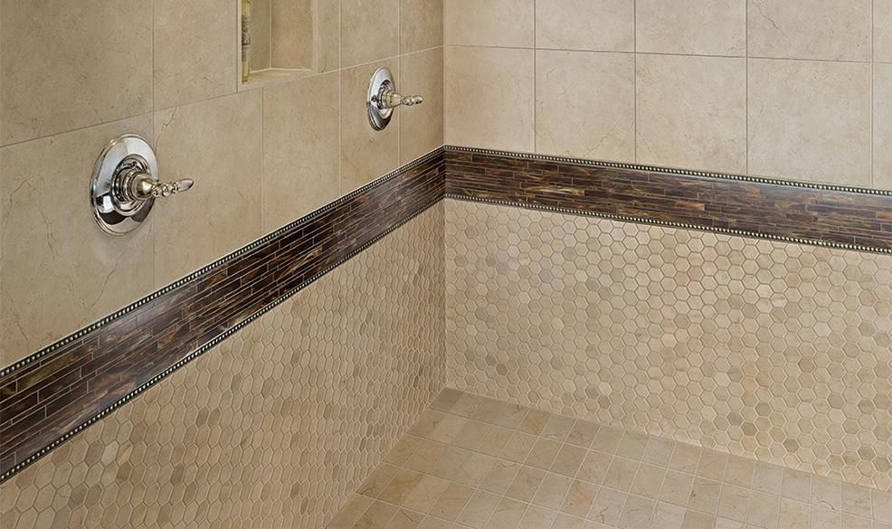 Tiled shower corner with beige walls, stone accent border, and chrome faucets