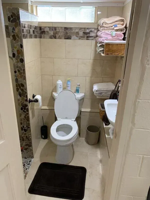 Small bathroom with toilet, sink, shelves of towels, and a black bath mat.