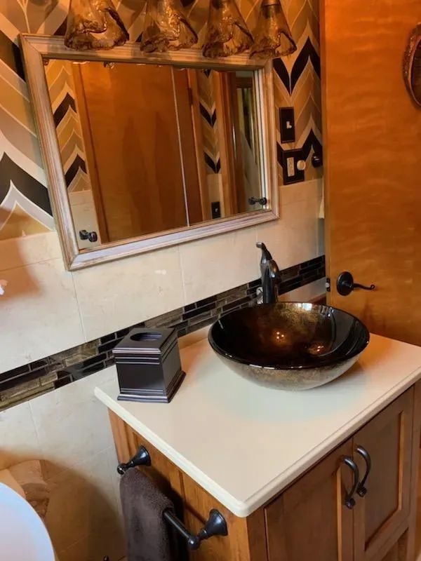 Bathroom vanity with mirror, black vessel sink, and white countertop in warm orange tones