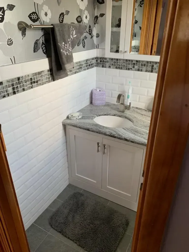 Small bathroom vanity with white subway tile, gray walls, and a mirror under warm lighting.