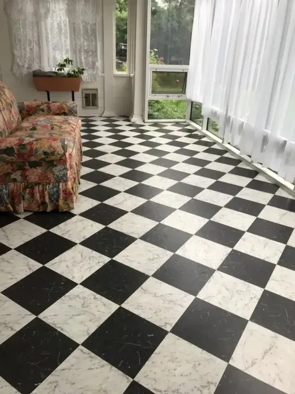 Sunlit room with black-and-white checkered floor, floral sofa, potted plant, and sheer curtains