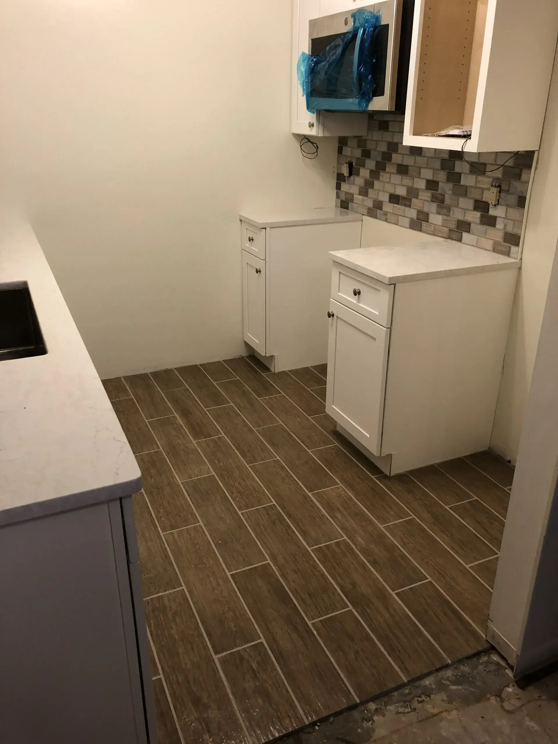 Empty kitchen with gray tile floor, white cabinets, and a small dishwasher under a mosaic backsplash.