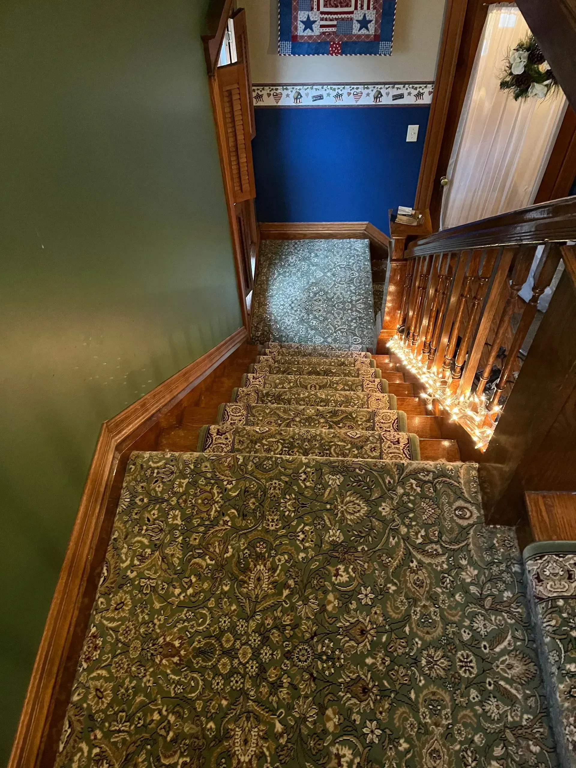 Carpeted staircase with wooden railings leading to a blue-walled hallway and doorway.