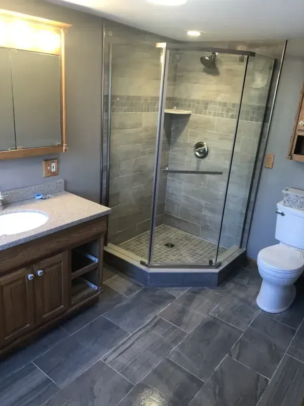 Modern bathroom with vanity, toilet, and glass-enclosed corner shower on dark tiled floor