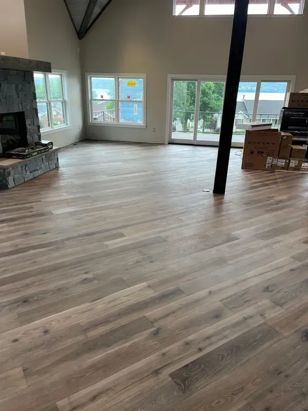 Empty modern living room with large windows, wood floors, stone fireplace, and a black support beam