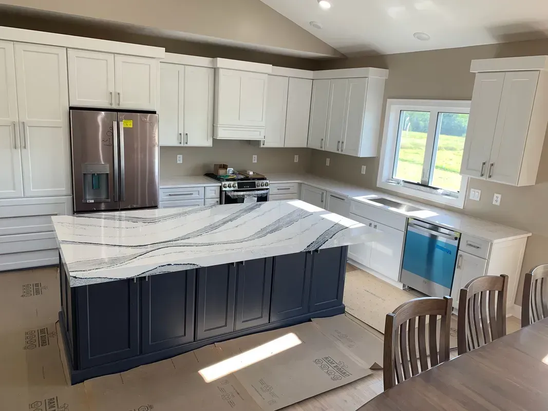 Modern kitchen with white cabinets, marble island, stainless fridge, and blue range hood