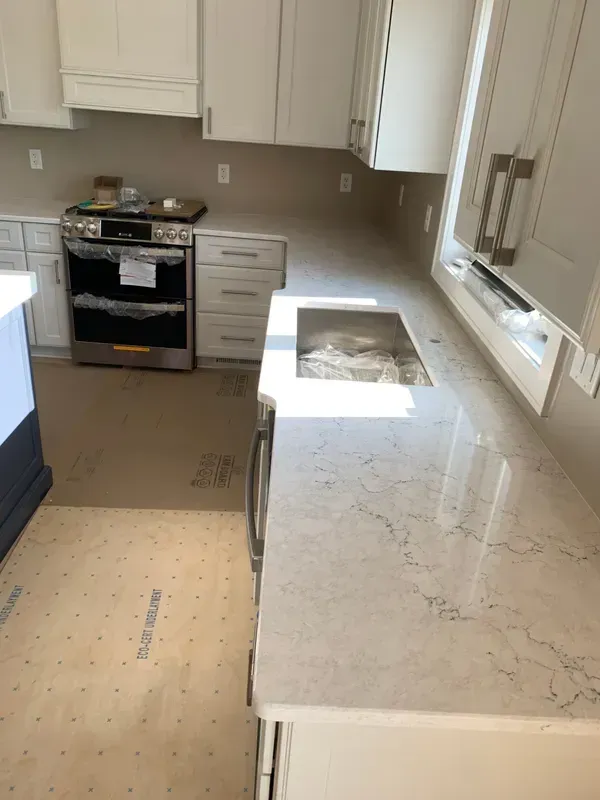 Renovated kitchen with white cabinets, marble island, and stove installed; floor partially unfinished.