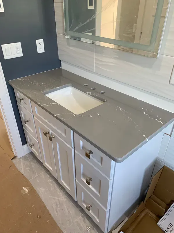 Bathroom vanity with white cabinets and gray countertop, sink cutout, and window behind it during renovation