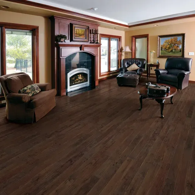Cozy living room with dark wood floors, fireplace, windows, and black and brown chairs