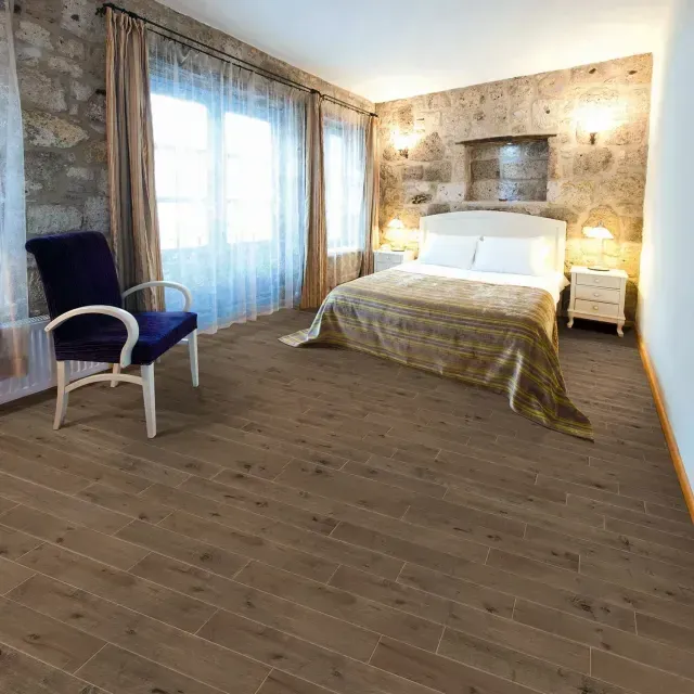Bright bedroom with stone walls, large windows, a bed, and a blue armchair on wooden floors